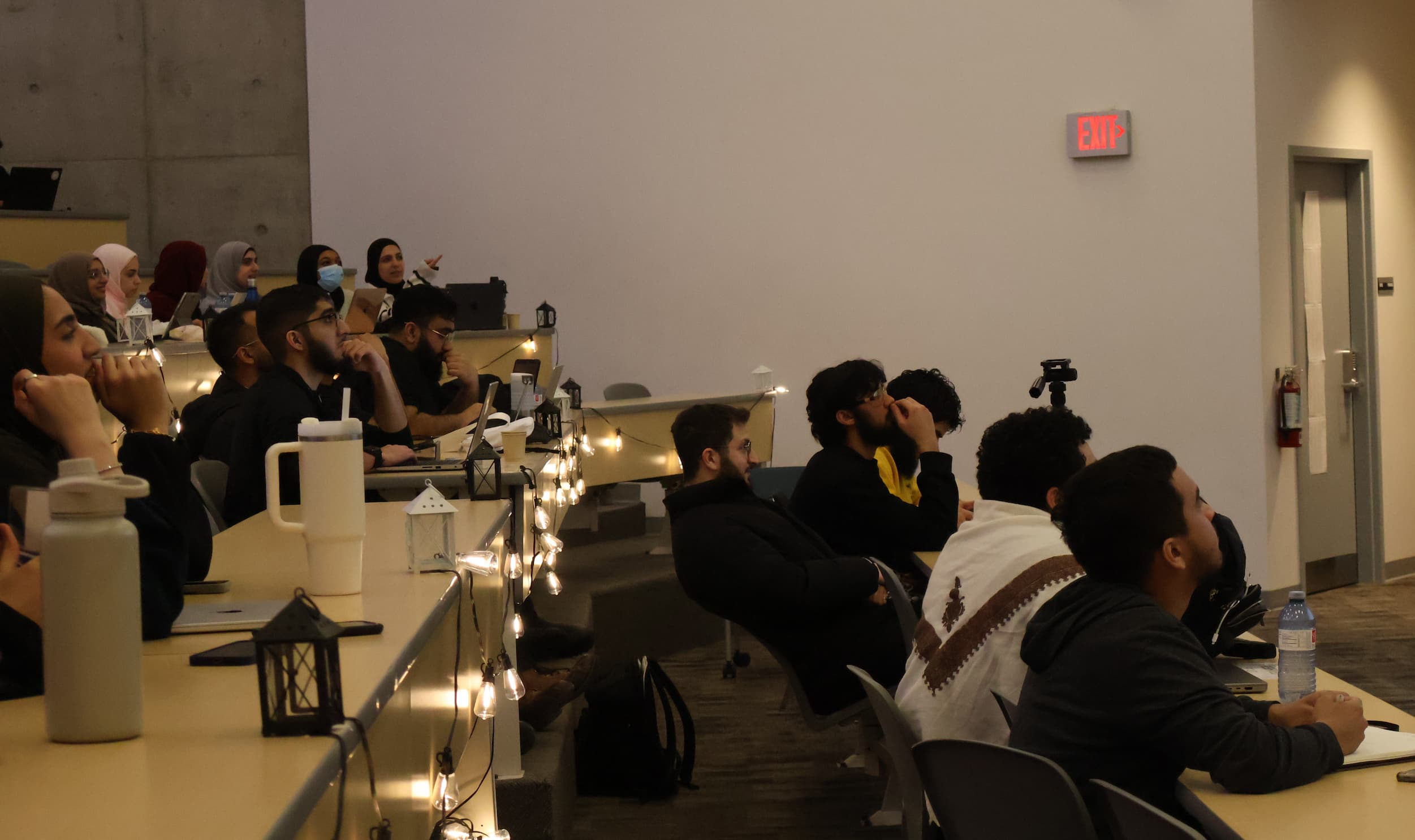 Students in a lecture hall listen to a talk being given by an individual off-screen.